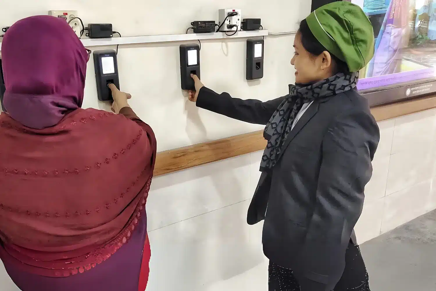 Two health staff checking in on wall-mounted Tipsoi attendance devices at a government health complex in Bangladesh