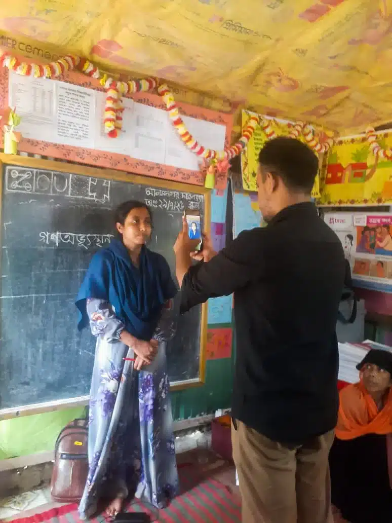 A BRAC teacher standing at the blackboard while her face is enrolled for attendance